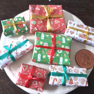 May include: Miniature Christmas presents wrapped in festive paper with ribbons. The gifts feature various holiday patterns, including candy canes, ornaments, and gingerbread men. The presents are arranged on a white surface, with a coin visible.