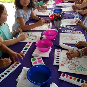 May include: A group of children are painting on canvases at a table covered in a purple tablecloth. They are using watercolors and paintbrushes. There are several bowls of water and paint palettes on the table.