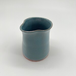 May include: A small, light blue ceramic jug with a slightly uneven rim and a light brown base.