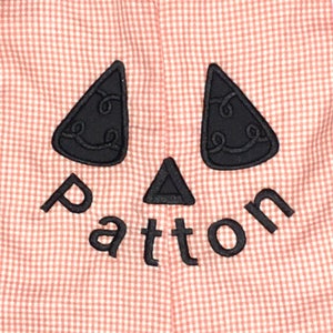 Puede incluir: Una tela de guingán rosa y blanca con una cara de calabaza tallada bordada en negro y el nombre "Patton" debajo.