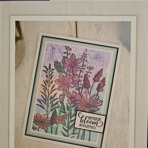 May include: An embossing folder by Crafter's Companion with a floral design. The image shows pink and purple flowers and the text "Bloom, May Your Day With Happiness." The folder size is 15.2cm x 10.2cm.