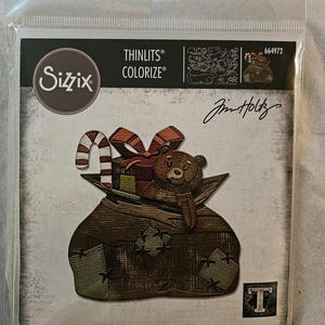 Könnte beinhalten: Ein Sizzix Thinlits Colorize Stanzformen-Set mit einem braunen Teddybären, Geschenken und einer Zuckerstange, die aus einem braunen Sack herausragen. Das Set enthält 17 Stanzformen. Die Verpackung trägt den Text "Jim Holtz".