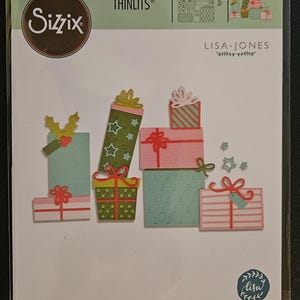Puede incluir: Juego de troqueles Sizzix Thinlits con diseños de cajas de regalo. El juego incluye cajas de regalo de varios tamaños y colores, con lazos y adornos decorativos. El embalaje incluye el texto "LISA JONES" y "21 DIES | 21 MATRICES | 21 TROQUELES | 21 FUSTELLE | 21 ВЫРУБКИ | 21 STANZEN | 21 CORTANTES".