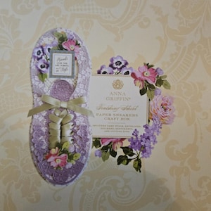 Könnte beinhalten: Eine dekorative Papiersneaker-Bastelbox mit floralem Design. Die Box hat die Form eines Schuhs und hat eine lavendelfarbene Farbe mit floralen Akzenten und einer Schleife. Die Box enthält den Text "Friends are always in style."