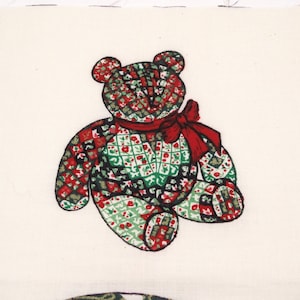 May include: A patchwork teddy bear with a red bow. The bear is made of green, red, and black fabric with a white background. The bear is sitting on a white background.