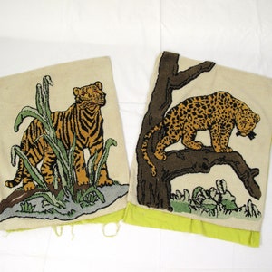 May include: Two embroidered throw pillows with animal motifs. One pillow features a tiger standing in tall grass, while the other pillow features a leopard perched on a tree branch. Both pillows have a cream background with green, brown, and yellow accents.