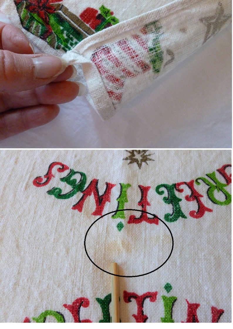 May include: White cotton tea towel with a red, green, and gold Christmas design. The towel has the words "Greetings" and "Holiday" printed on it. There is a small yellow stain on the towel.