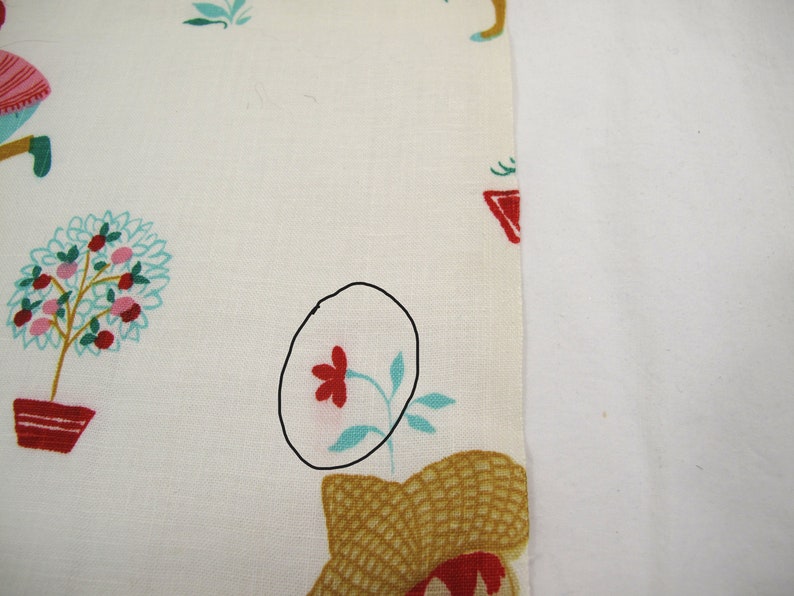 May include: White fabric with a red flower and green leaves printed on it. The flower is outlined in black.