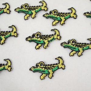 May include: Ten green and yellow embroidered alligator patches. The alligator patches are approximately 2 inches long and 1 inch wide. The patches are perfect for adding a fun and whimsical touch to clothing, bags, or other accessories.