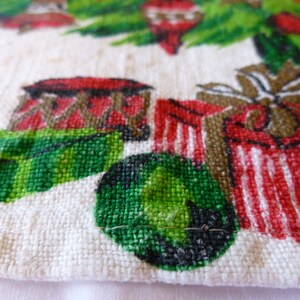May include: A white cotton tea towel with a Christmas-themed design. The design features a green Christmas tree with red and white ornaments, red and white striped presents, and a green and black ball.