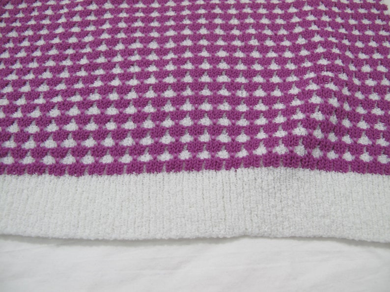 K&ouml;nnte beinhalten: Nahaufnahme eines gestrickten Stoffes mit einem wei&szlig;en und violetten geometrischen Muster. Der Stoff hat eine weiche, flauschige Textur.