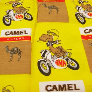 May include: Yellow fabric with repeating patterns of a camel riding a motorcycle and a camel illustration. The fabric also features the text "CAMEL FILTERS" in a white and red design.