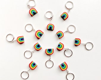 Può includere: Una collezione di portachiavi a forma di arcobaleno disposti su una superficie bianca. Ogni portachiavi presenta un design arcobaleno in miniatura con colori vivaci, tra cui rosso, arancione, giallo, verde, blu e viola. I portachiavi hanno un anello color argento.