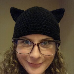 May include: A woman wearing a black crocheted cat ear beanie and glasses.