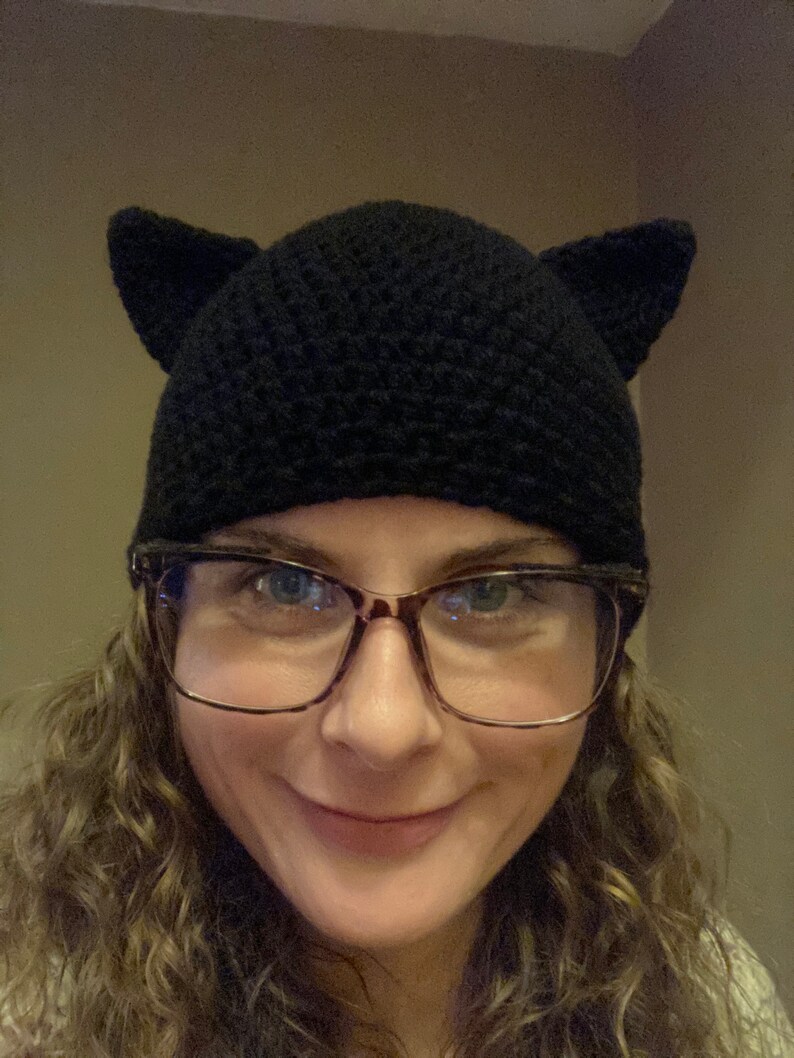 May include: A woman wearing a black crocheted cat ear beanie and glasses.