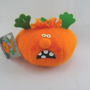 May include: An orange plush pumpkin with a surprised expression, white teeth, and green leaf accents. The pumpkin has a tag that reads "Your Wacky Patch". A fun, whimsical Halloween decoration.