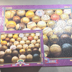 May include: A jigsaw puzzle featuring a collage of vintage baseballs, some with visible numbers. The puzzle is framed in a purple border with the words "The Old Ball Game". A smaller, completed puzzle is also present.
