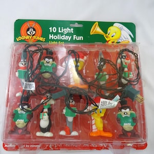 May include: A Looney Tunes 10-light holiday light set in a clear plastic package. The lights feature cartoon characters like Bugs Bunny, Tweety Bird, and Taz. The package has a green header with the Looney Tunes logo and the words "10 Light Holiday Fun".