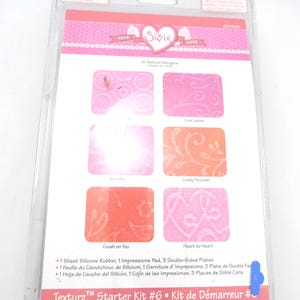 May include: A clear plastic package containing a Texturz Starter Kit #6. The kit includes a silicone rubber sheet, an impressions pad, and double-sided plates. The packaging features pink and orange designs with the Sizzix logo and the words "TRUE LOVE".