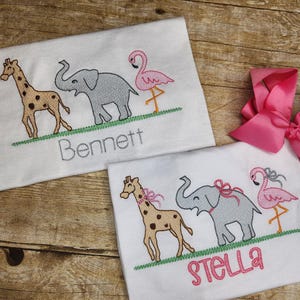 May include: Two white t-shirts with embroidered images of a giraffe, elephant, and flamingo. The shirts are personalized with the names "Bennett" and "Stella".