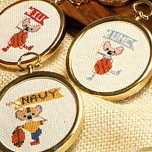 Puede incluir: Cinco llaveros de color dorado con imágenes bordadas de animales de dibujos animados que sostienen carteles con texto. Los carteles dicen "JUI", "JUNE", "UDLA", "NAVY" y "CHS".