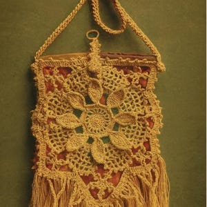Pode incluir: Bolsa de crochê bege feita à mão com design floral e franjas. A bolsa apresenta uma alça longa e um padrão floral decorativo no centro. A bolsa é feita de um fio macio e texturizado e tem uma estética vintage.