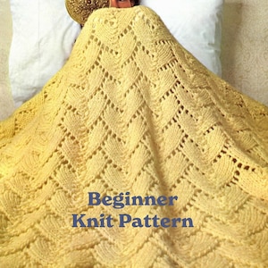 May include: A yellow knitted blanket with a lacy pattern. The blanket is draped over a bed and the text "Beginner Knit Pattern" is visible in the center of the image.