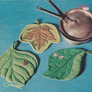 May include: Three leaf-shaped pot holders, one brown, one green with a ladybug, and one green with a dragonfly. The pot holders are on a blue background with a copper pot in the background.
