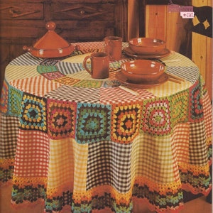 May include: A round tablecloth with a checkered pattern in red, yellow, and black. The tablecloth has a crocheted border with colorful squares in shades of green, blue, orange, and brown. The tablecloth is set with a brown ceramic pot, two mugs, and two bowls.