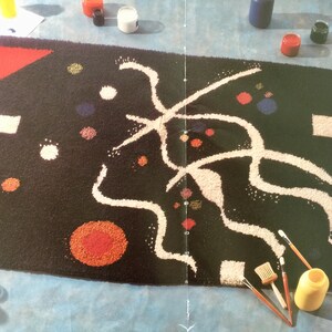 May include: A black rug with a white abstract design and colorful dots. The rug is being painted with brushes and paint.
