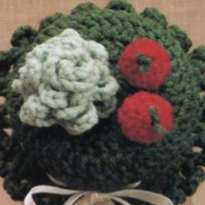 May include: A green crocheted jar lid cover with a white crocheted flower and two red crocheted tomatoes on top. A white satin ribbon is tied around the base of the lid.