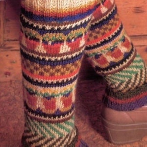 Könnte beinhalten: Ein Paar bunte gestrickte Beinstulpen mit geometrischem Muster. Die Beinstulpen sind aus verschiedenen Farben gefertigt, darunter Rot, Orange, Gelb, Grün, Blau und Braun. Die Beinstulpen werden über einem Paar brauner Schuhe getragen.