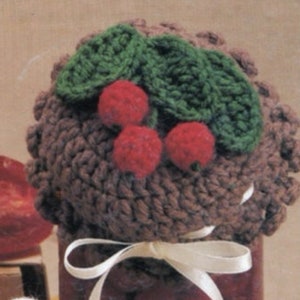 May include: A brown crocheted jar lid with a white ribbon and a crocheted cherry design on top. The cherries are red and the leaves are green.