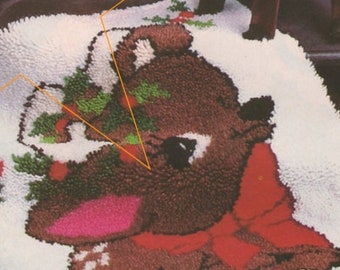 May include: A white rug with a brown and pink reindeer wearing a red bow and holding a sprig of holly.