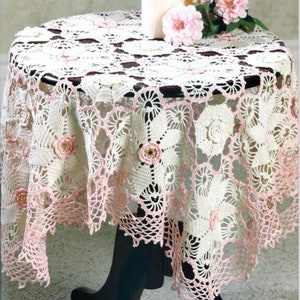 May include: A white and pink crocheted table cloth with a floral design. The tablecloth has a scalloped edge and is decorated with small pink flowers.