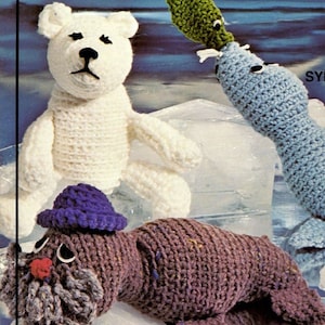 May include: A crocheted white polar bear named "FRIGIE", a blue crocheted seal named "SYLVESTER", and a brown crocheted walrus named "WAFFLES" on a background of ice.