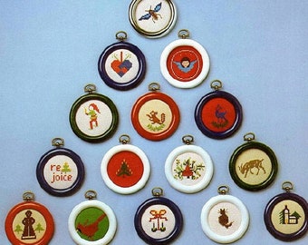 May include: A collection of 16 round, framed, cross-stitch ornaments with various Christmas themes. The ornaments are arranged in a Christmas tree shape on a light blue background. The ornaments feature designs such as a cardinal, a snowman, a reindeer, a Christmas tree, a bell, and a heart.