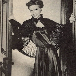 Puede incluir: Una mujer con un vestido negro con una superposición de encaje se encuentra en una puerta. Lleva un vestido negro con una superposición de encaje y tiene la mano en el marco de la puerta.