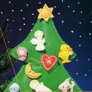 Puede incluir: Un adorno de árbol de Navidad de fieltro con un árbol de fieltro verde, una estrella amarilla, un ángel blanco, una flor rosa, un corazón rojo, una luna creciente amarilla, un bebé Jesús blanco, un pájaro azul y un pez rosa.