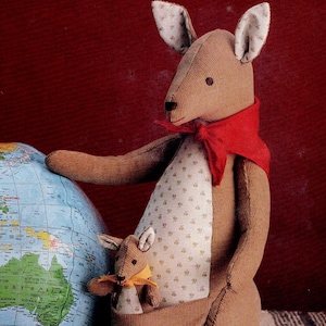 May include: A brown stuffed kangaroo with a red scarf and a baby kangaroo in its pouch. The kangaroo is holding a globe. The kangaroo's pouch is lined with a patterned fabric. The background is a dark red.