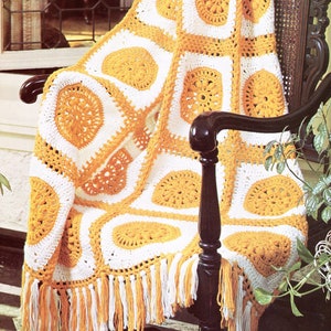 May include: A crocheted throw blanket with a white and yellow geometric pattern. The blanket has fringe on the bottom edge and is draped over a wooden chair.