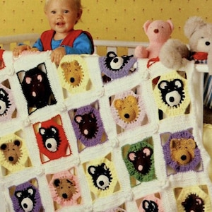 May include: A white crib with a crocheted baby blanket featuring a repeating pattern of bear faces in various colors. The blanket is hanging over the side of the crib. A baby is sitting on the edge of the crib, looking at the camera.