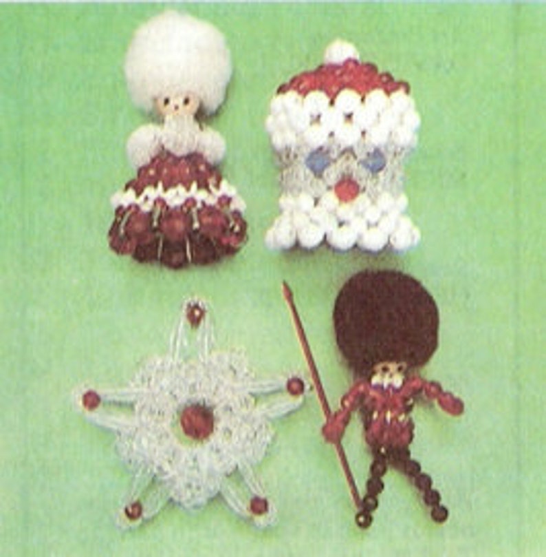 Op de afbeelding: Vier handgemaakte kralenornamenten op een groene achtergrond. De ornamenten omvatten een pop met een witte, donzige kop en een rood-witte jurk, een kerstmanfiguur, een ster en een soldaat met een speer.