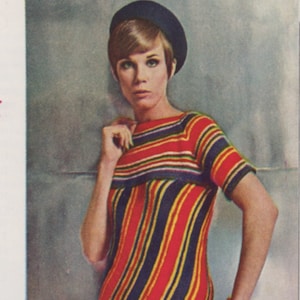 May include: A woman wearing a striped, red, yellow, blue, and black knit dress with a black beret.