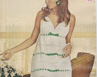 May include: A white crochet dress with green ribbon trim and a bow at the waist. The dress is sleeveless and has a V-neckline. The model is wearing the dress and has long brown hair.