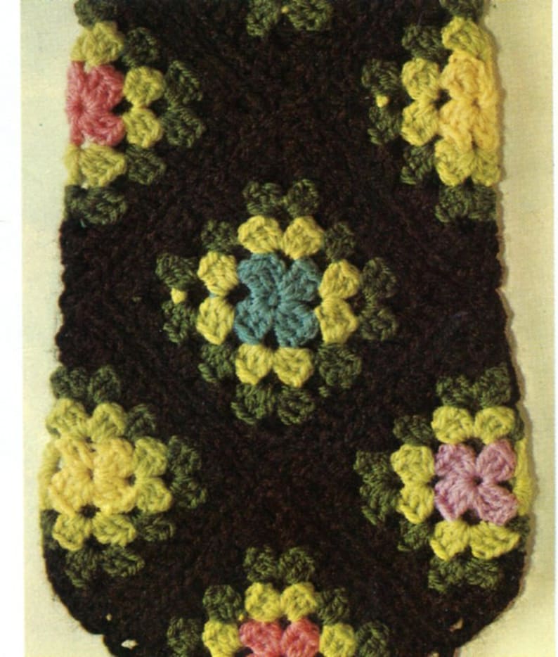 May include: A brown crocheted fabric with a repeating pattern of colorful flowers. The flowers are yellow, pink, green, and blue.