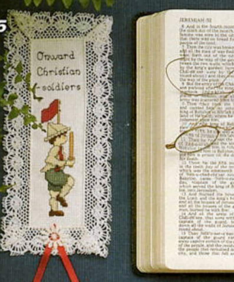 May include: A white lace bookmark with a cross-stitch design of a young boy in a red hat holding a flag. The text "Onward Christian Soldiers" is embroidered on the bookmark.