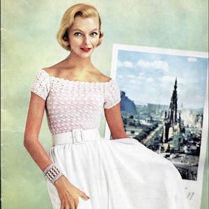 May include: A short-sleeved, off-the-shoulder top with a light pink, textured, scalloped knit pattern. The top is paired with a solid white, high-waisted skirt featuring a wide white belt with a rectangular buckle and a multi-strand beaded bracelet.