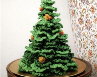 Op de afbeelding: Een gehaakte kerstboom in groen met een gelaagde, geplooide textuur. De boom is versierd met kleine, ronde, getextureerde oranje en gele ornamenten die over de takken verspreid zijn, wat zorgt voor een zachte, handgemaakte uitstraling.