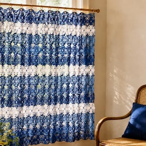 May include: A rectangular crochet curtain featuring alternating horizontal stripes of deep blue and white yarn. The fabric displays a repeating circular openwork pattern throughout, suspended from a wooden rod by metal rings at the top edge.